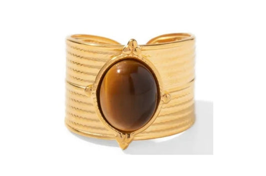 Close up frontal view of bold statement ring that features a striking tiger's eye center stone set in a luxurious gold-plated, tarnish resistant, long lasting stainless steel band. The thick adjustable band adds a touch of drama, making it the perfect accessory for those who dare to stand out.